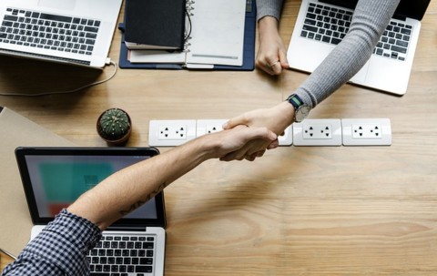 shaking hands across desk over laptops