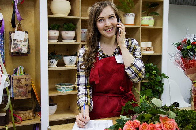 woman wearing red apron taking holiday phone order in flowershop