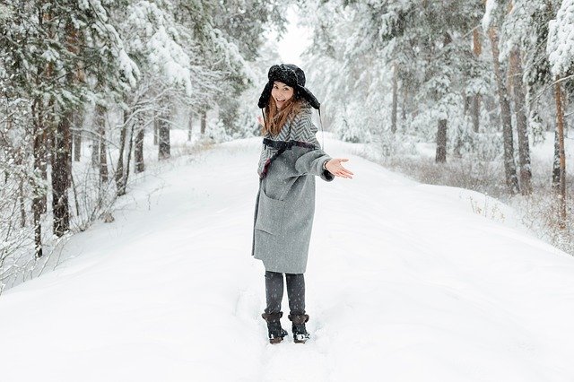Girl in snow wearing black hat and grey long coat