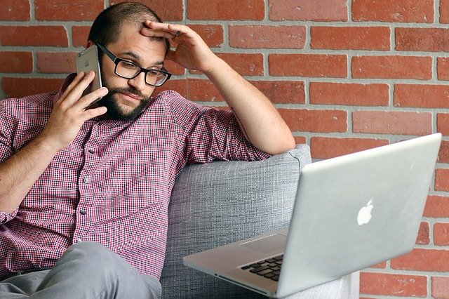 frustrated man in red plaid dress shirt on cell looking at macbook_stevedimatteo