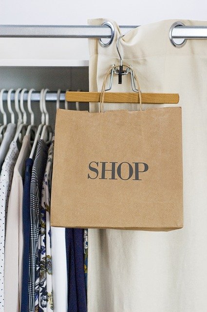 brown shopping bag with SHOP on it hanging next to sales rack of clothes